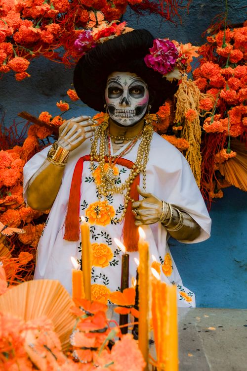 Free A person in traditional Dia de los Muertos attire surrounded by bright marigolds and decorations. Stock Photo
