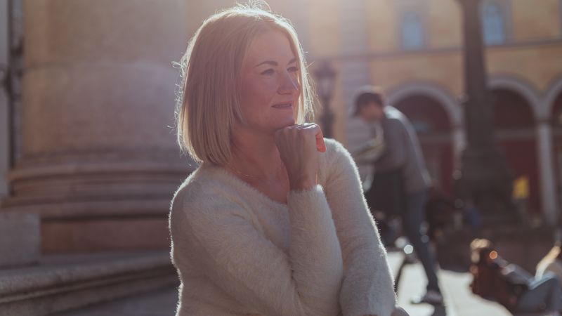 A mature woman taking a quiet moment outdoors in warm natural light.