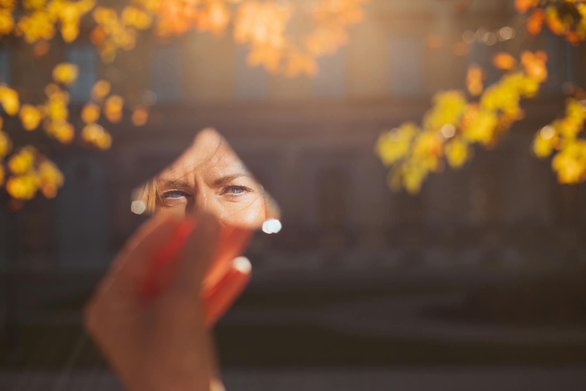 A person holding a mirror reflects autumn leaves in a München park.