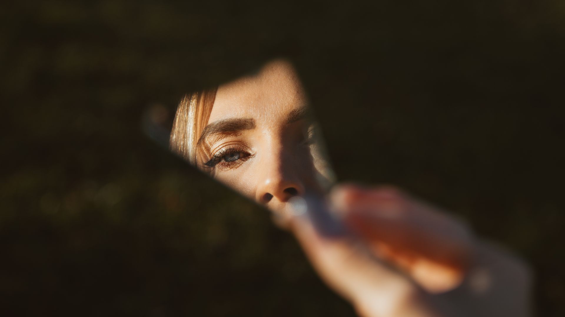 Close-up of a woman's eye seen through a mirror fragment outdoors.