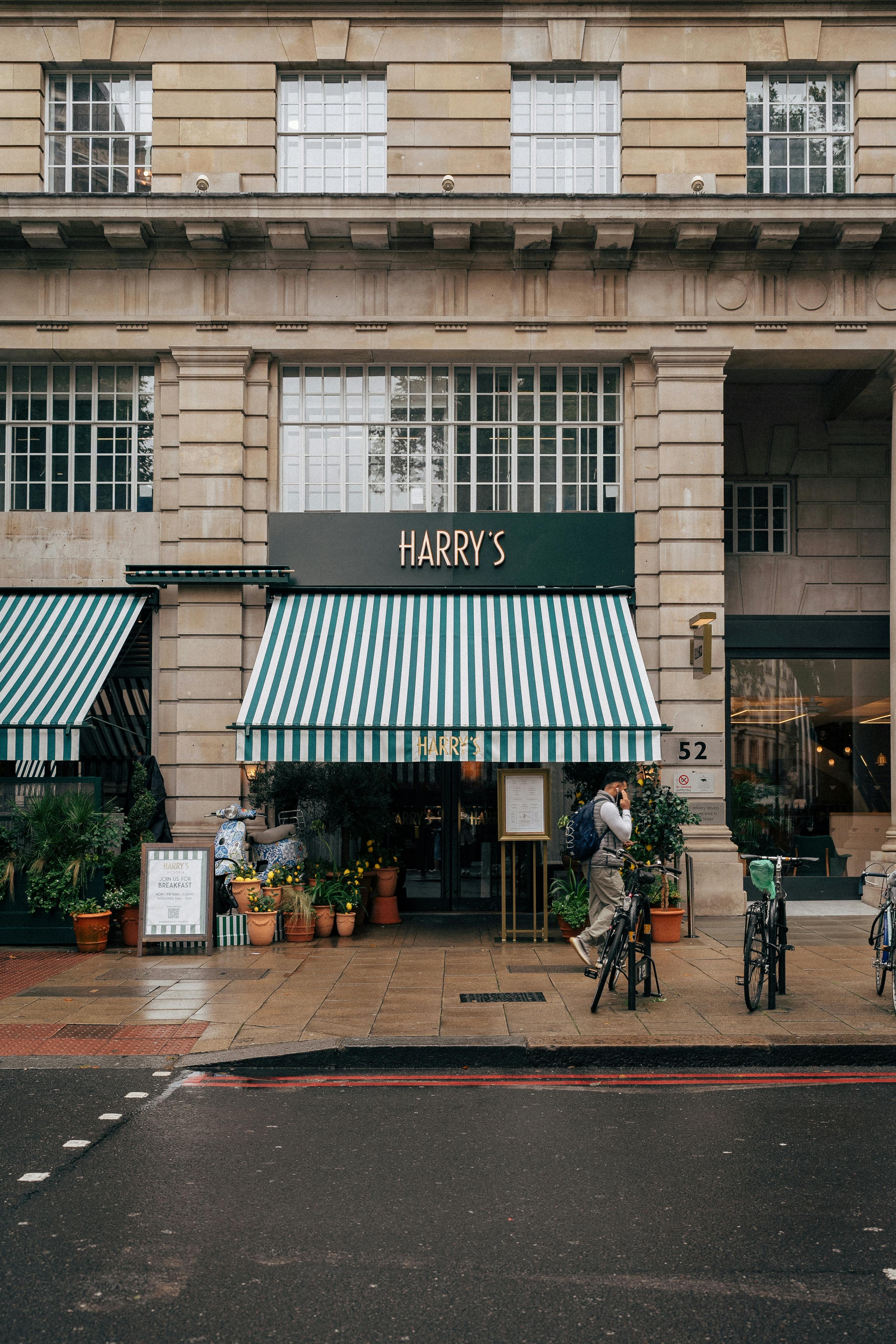 Street view of Harry's cafe entrance in London with striped awning and potted plants.