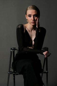 Moody portrait of a woman in dark attire sitting on a chair.