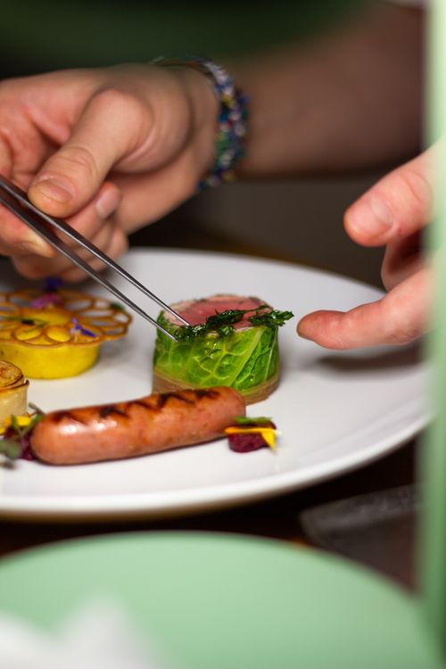 Free Chef arranging gourmet dish with sausage, cabbage roll, and delicate garnishes on a white plate. Stock Photo