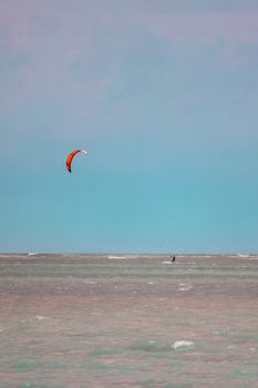 A lone kitesurfer skillfully rides over the ocean waves under a clear blue sky.