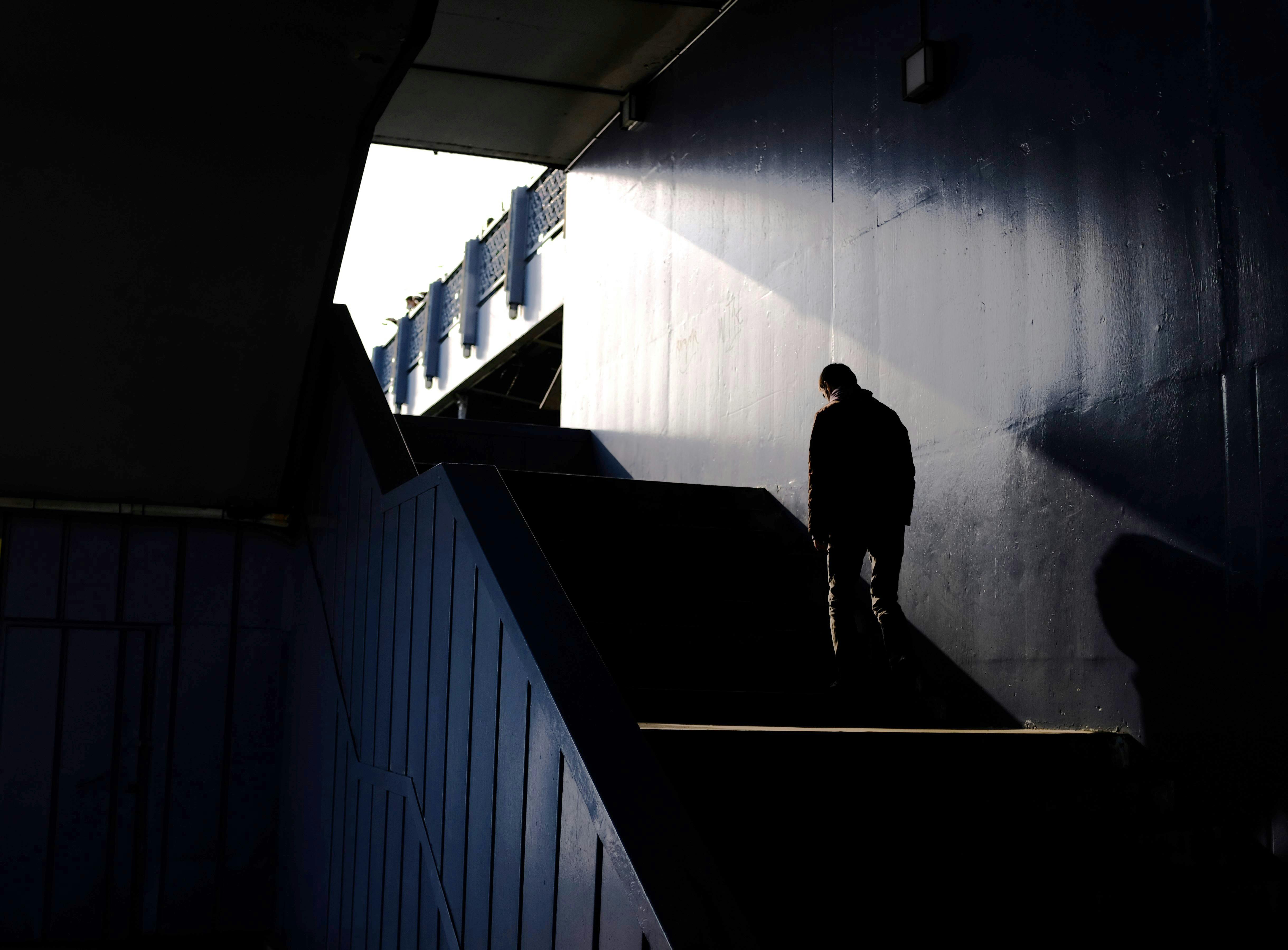 A lone figure in silhouette walks up a shadowy staircase, creating a dramatic light contrast.
