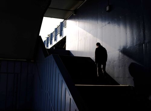Free A lone figure in silhouette walks up a shadowy staircase, creating a dramatic light contrast. Stock Photo