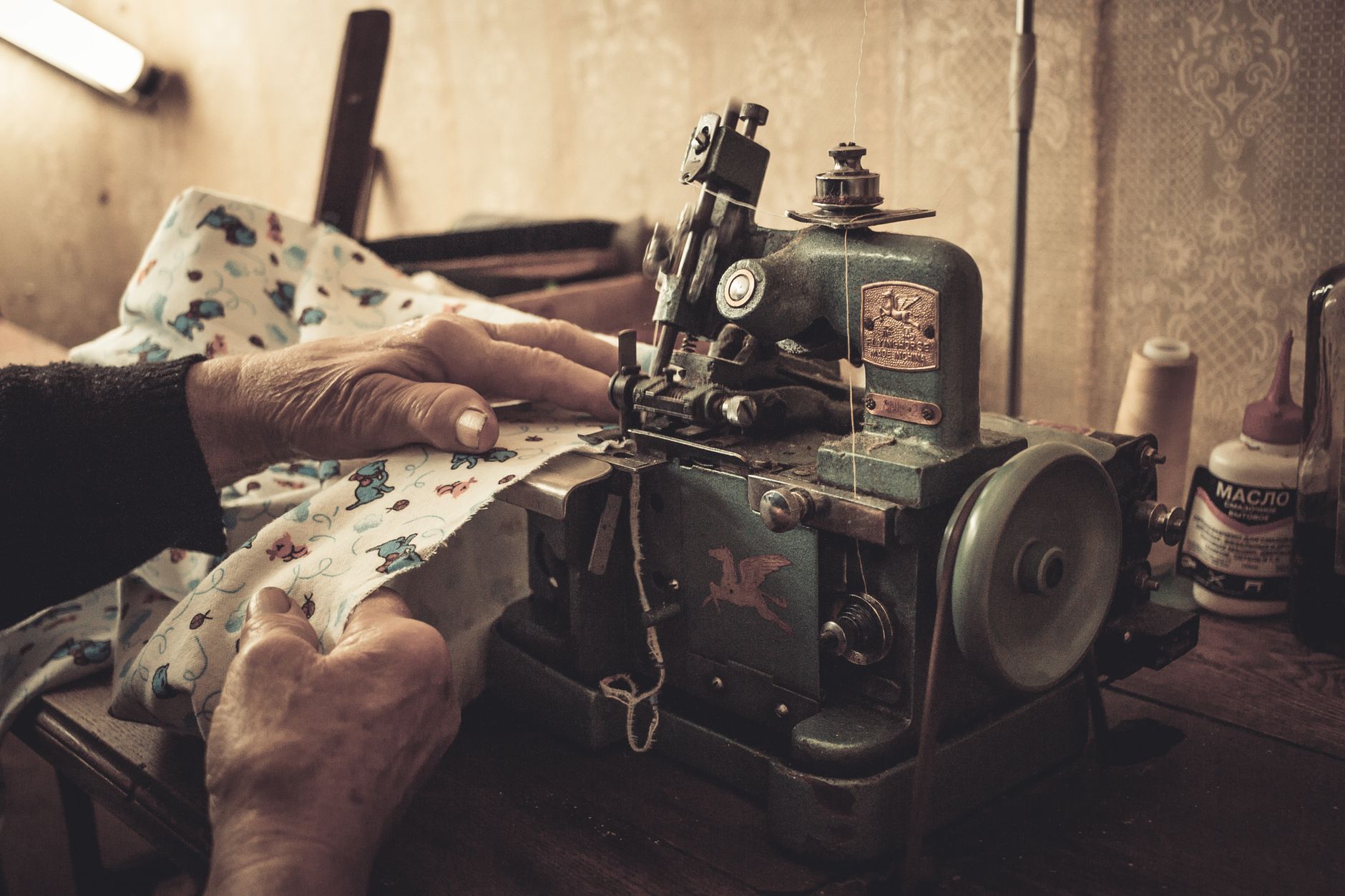 Close-up of hands sewing with a vintage machine in a dimly lit room.