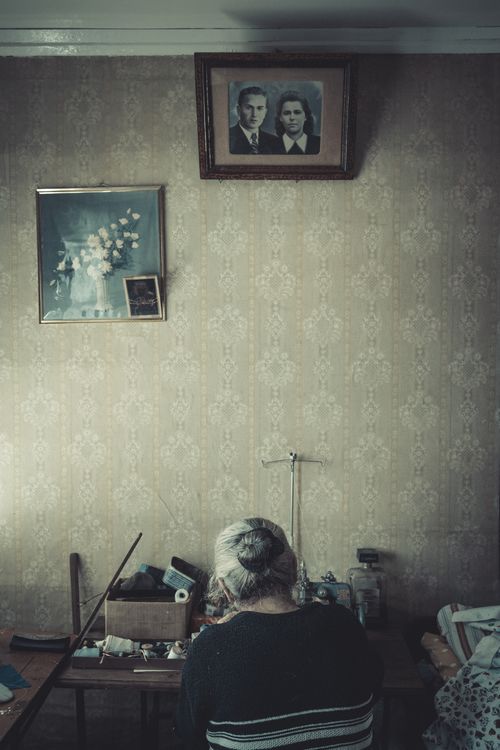 Free Elderly woman crafting in a vintage room with old photographs and wallpaper. Stock Photo