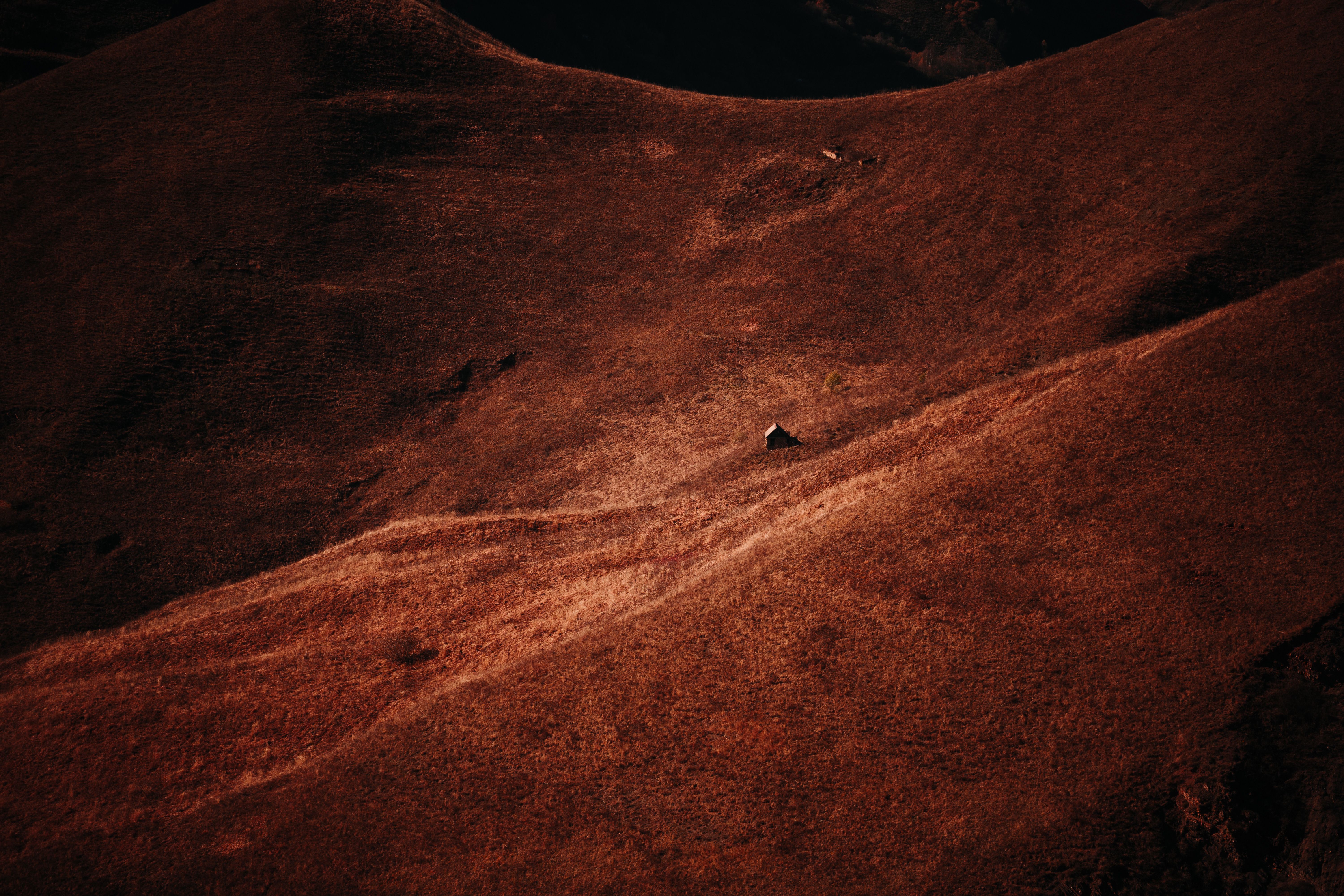 Aerial view of a solitary cabin surrounded by vast brown hills, capturing natural solitude.