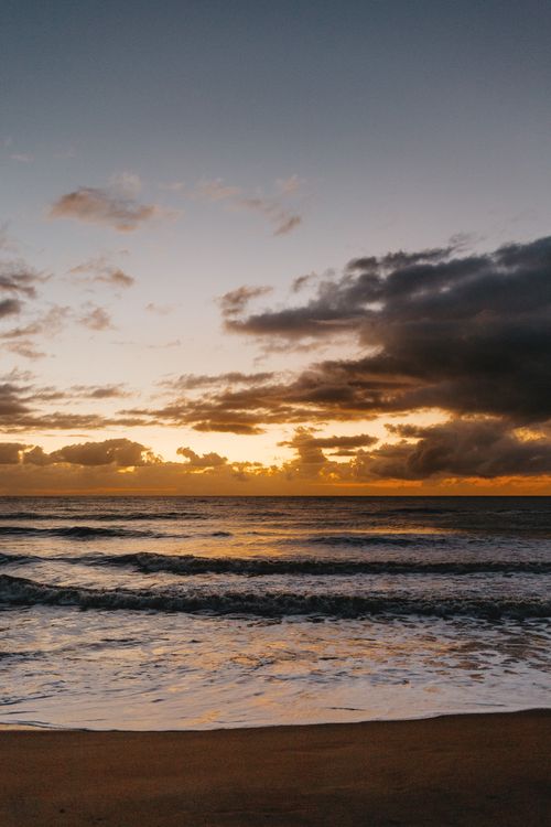 Free Golden sunset over ocean waves with dramatic clouds, perfect for nature and landscape themes. Stock Photo