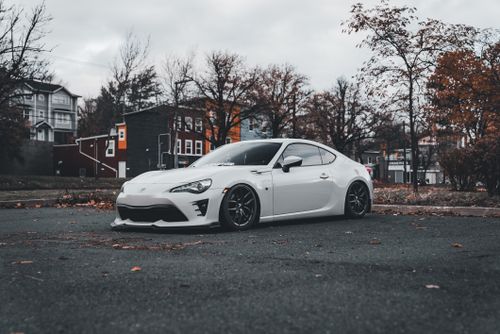 Free A sleek white sports car parked on an urban street surrounded by autumn foliage and residential buildings. Stock Photo