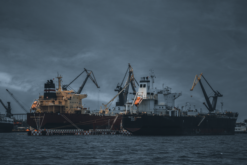 Cargo ships at a bustling port under cloudy skies, cranes ready for loading.