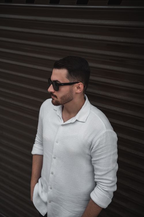 Free Man wearing sunglasses and a white shirt, leaning against a dark corrugated wall. Stock Photo