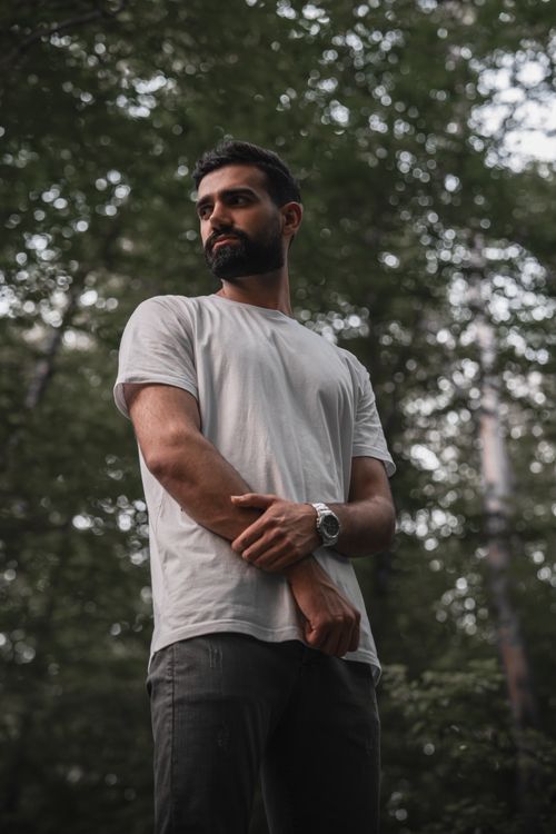 Free A man stands thoughtful in a forest with dappled sunlight. Stock Photo