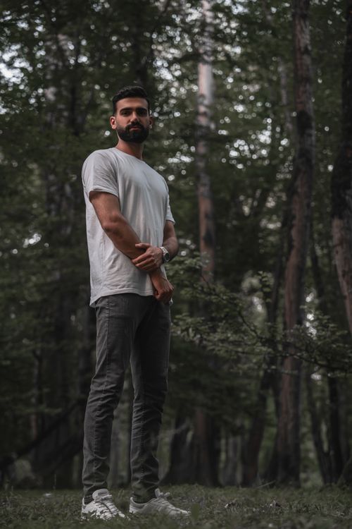Free A man standing confidently amidst a dense, serene forest backdrop. Stock Photo
