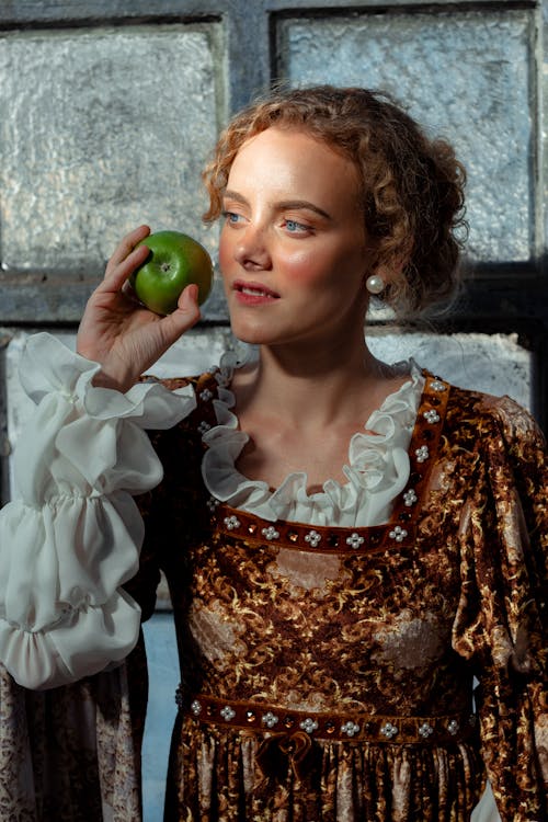 Dreamy woman in historical costume with apple near window