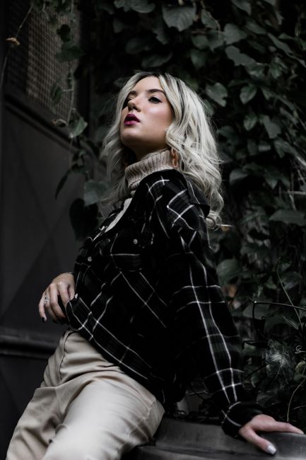 Stylish woman posing outdoors in plaid jacket and beige sweater.