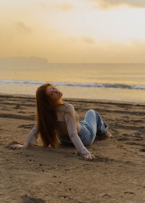 Free A young woman relaxes on a sandy beach, enjoying a tranquil sunset by the sea. Stock Photo
