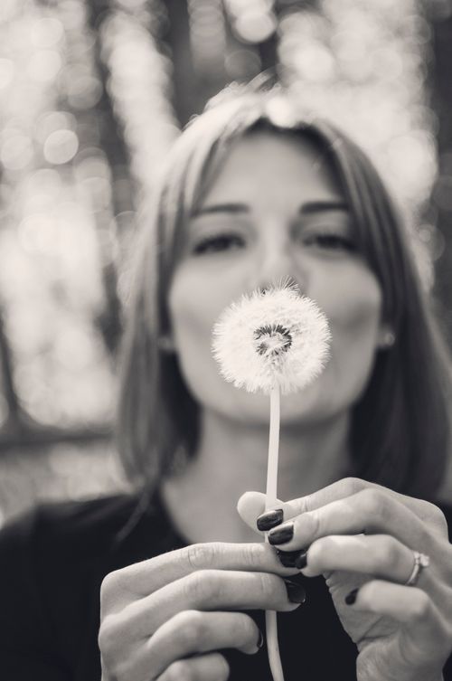 Free A woman holding a dandelion outdoors, captured in black and white for a moody effect. Stock Photo