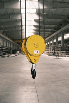 Closeup of a yellow crane hook with 5 ton weight limit in an empty industrial warehouse.