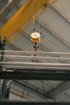 Close-up of an industrial crane hook lifting metal beams in a warehouse.
