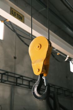 Close-up of a yellow industrial hook and pulley system in a workshop, highlighting lifting equipment.