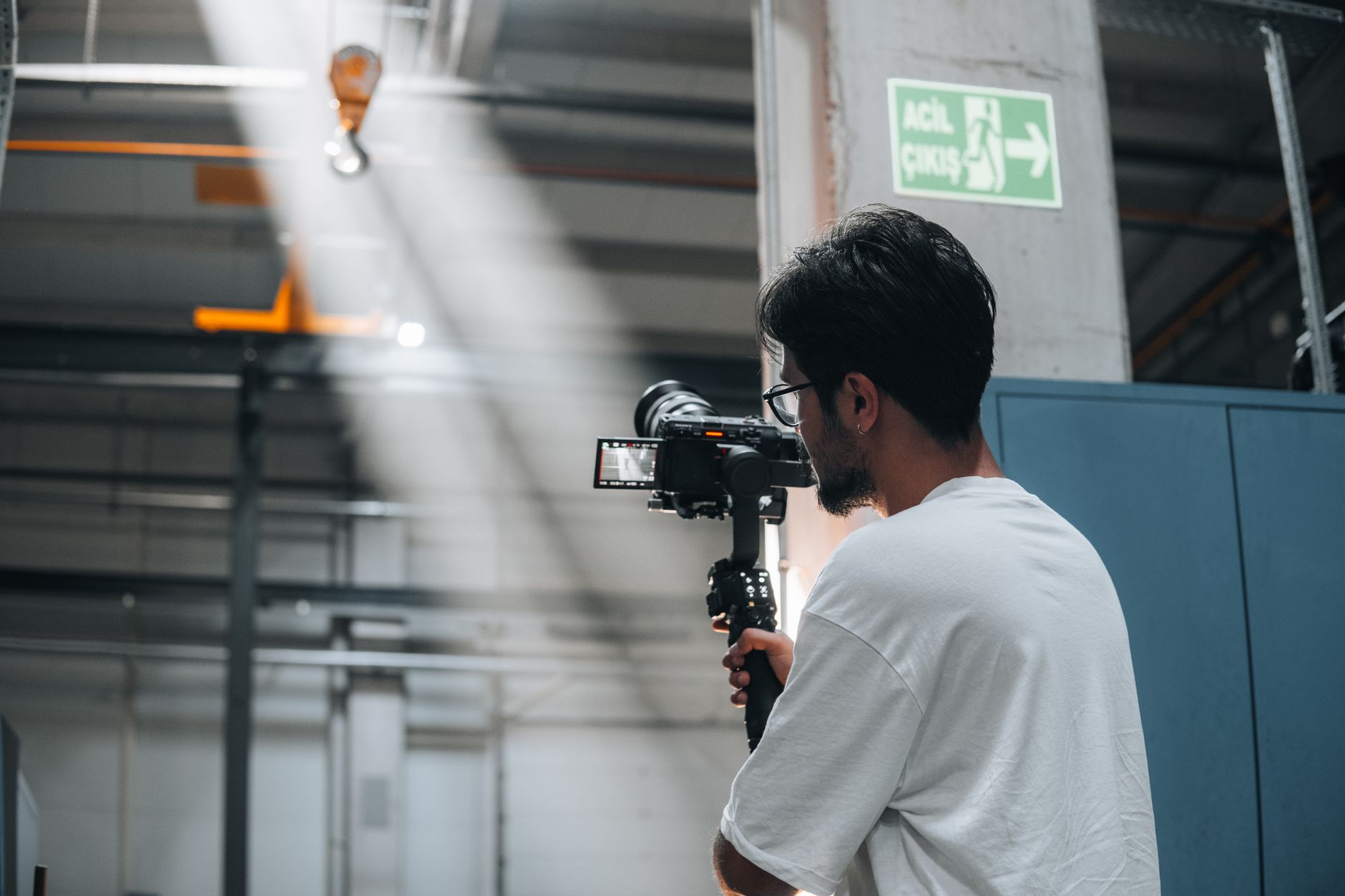 Cameraman using a gimbal to record a scene in an industrial interior space.