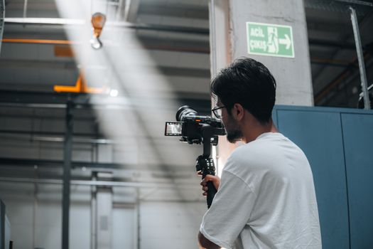 Cameraman using a gimbal to record a scene in an industrial interior space.