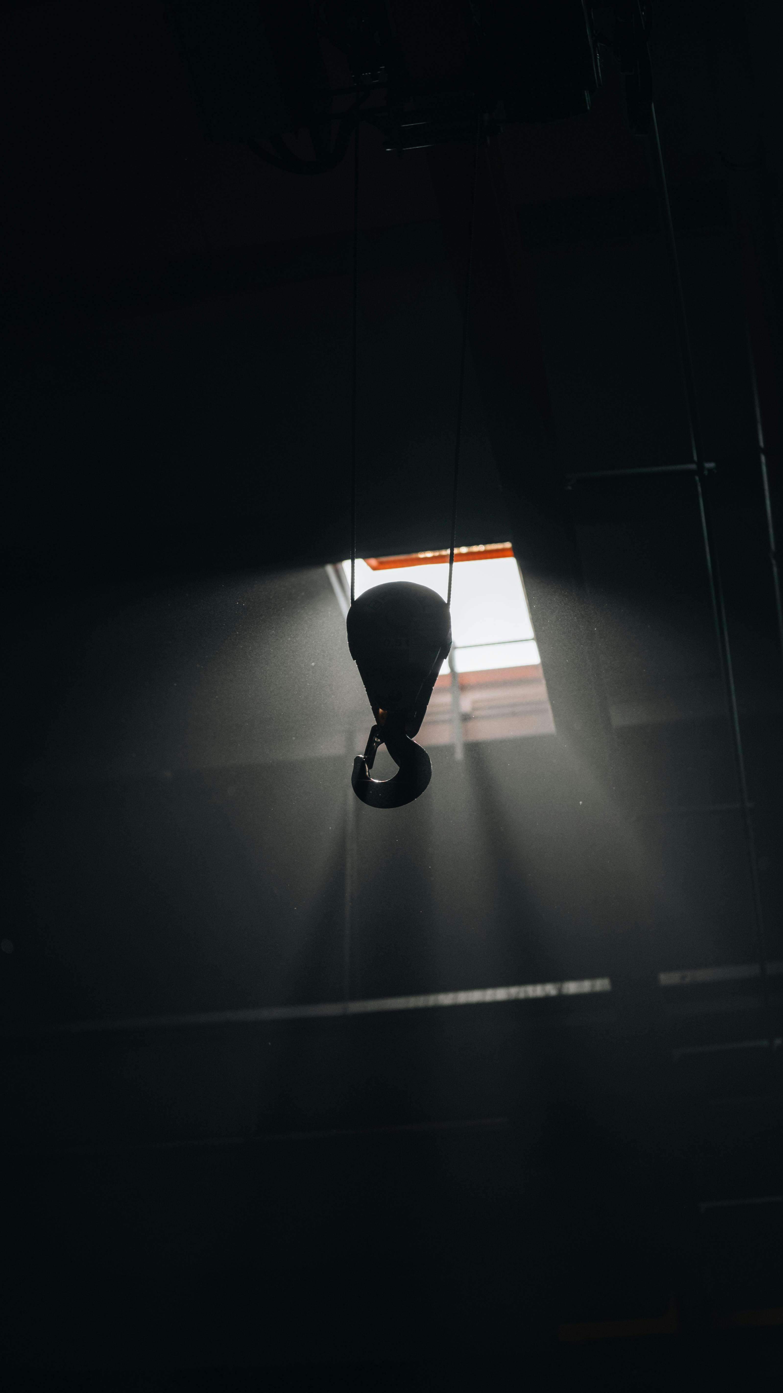 grátis Um gancho de metal suspenso em ambientes internos, iluminado por uma iluminação dramática, captura a força industrial. Foto profissional