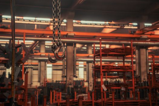 Interior of an industrial warehouse featuring overhead crane hooks and stacked metalwork.