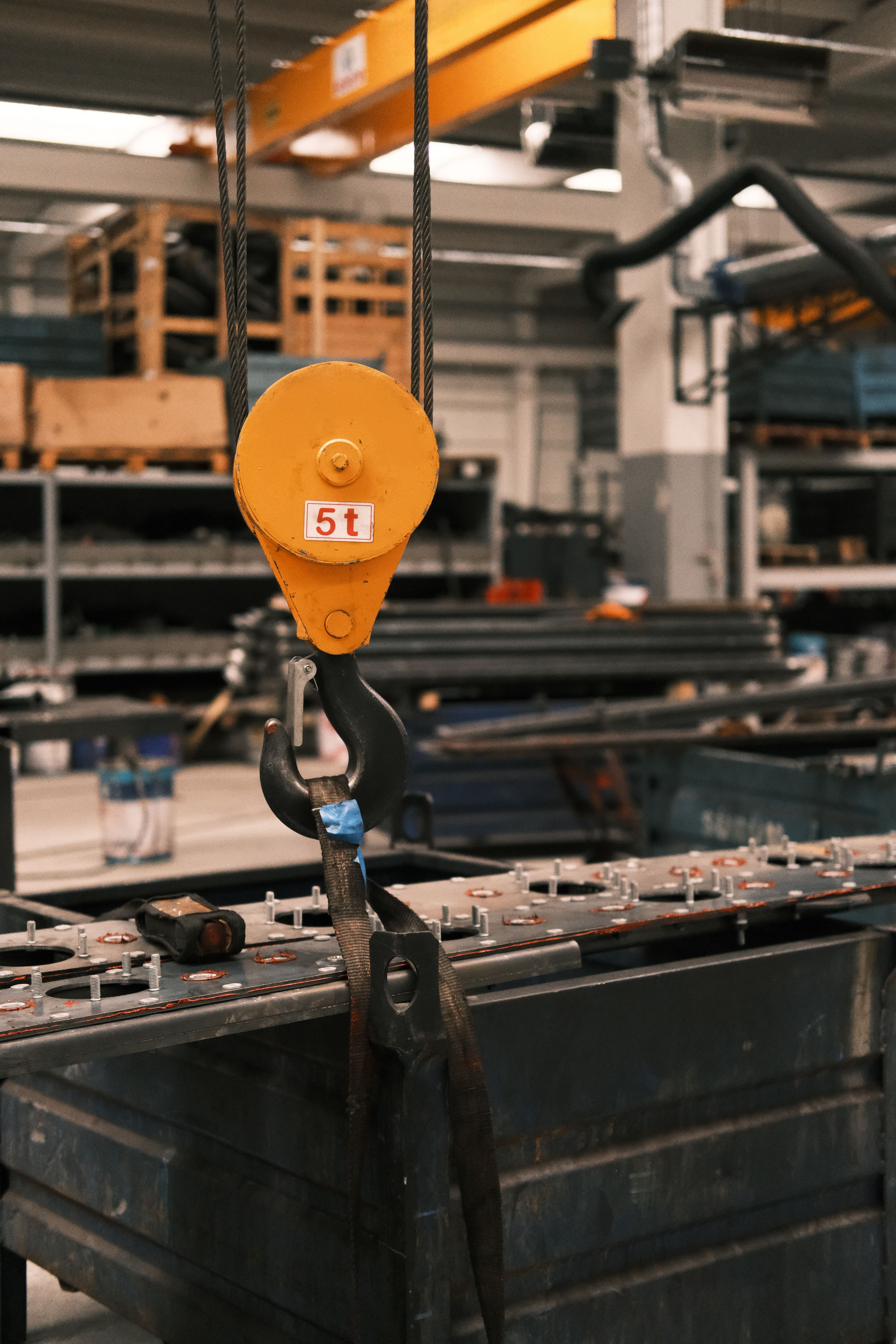 Yellow industrial hook lifting a 5-ton load in a factory setting.