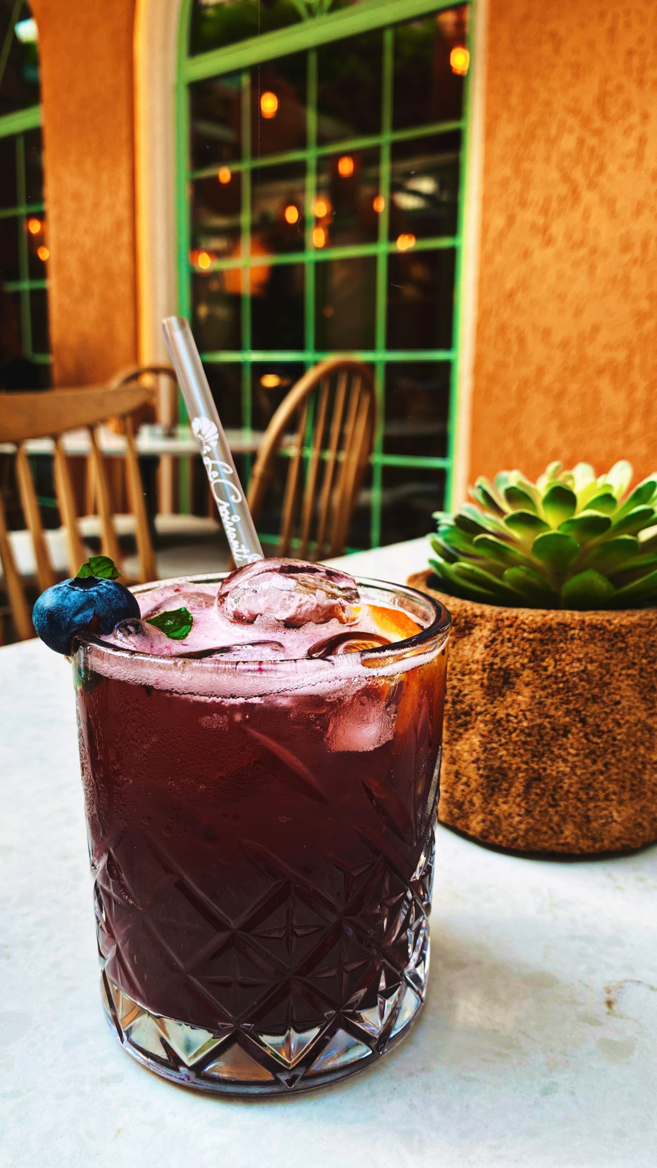 A vibrant blueberry cocktail with a straw, next to a succulent plant on a patio table.