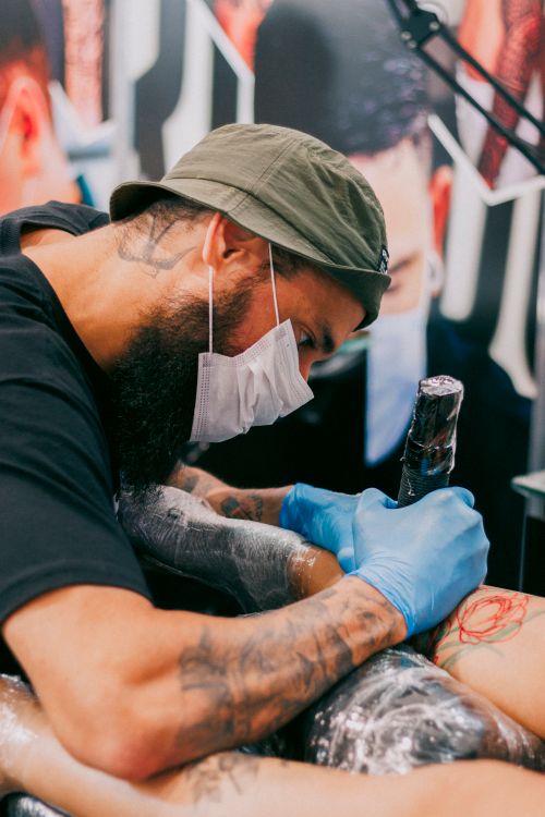 Free Tattoo artist wearing gloves and mask drawing an elaborate design on client's arm. Stock Photo