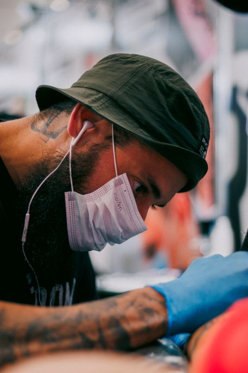 Free Close-up of a tattoo artist at work, wearing a face mask and gloves. Stock Photo