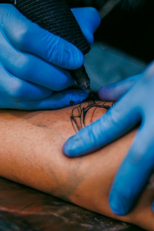 Free Tattoo artist wearing gloves working on intricate design on client's arm. Stock Photo