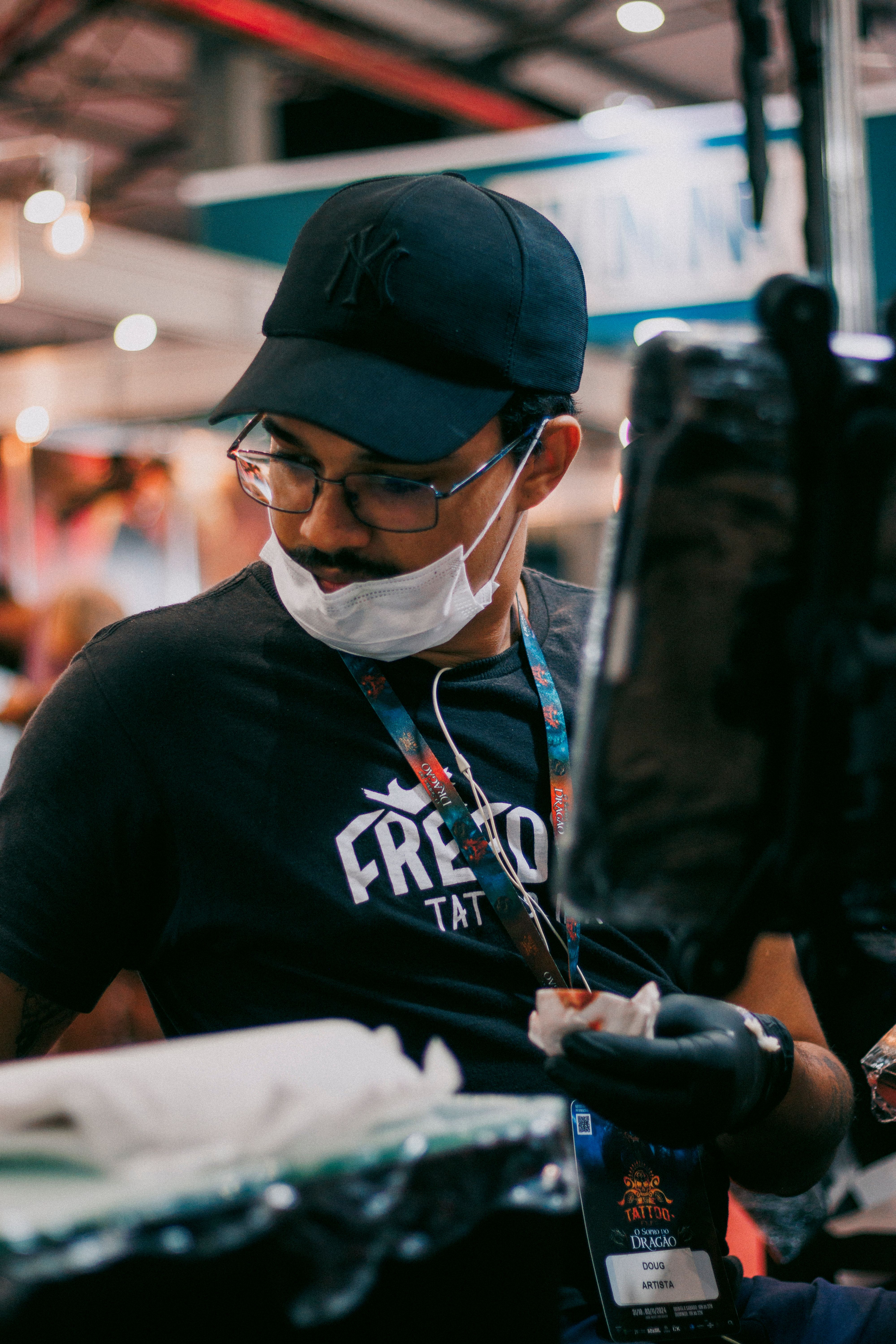 Tattoo artist in action with mask, focused and equipped indoors.