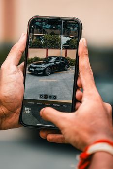 Hands holding a smartphone capturing a car image in a parking lot.