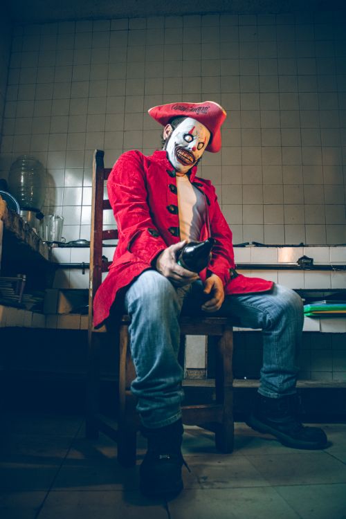 Free A person in a colorful clown pirate costume sits indoors, exuding a creepy and artistic vibe. Stock Photo