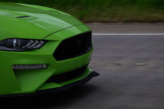Close-up of a green sports car driving on an empty road, showcasing sleek design and powerful headlights.