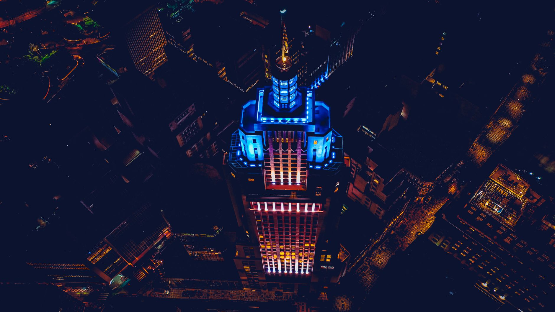 Aerial view of an iconic skyscraper illuminated at night with vibrant blue and red lights.