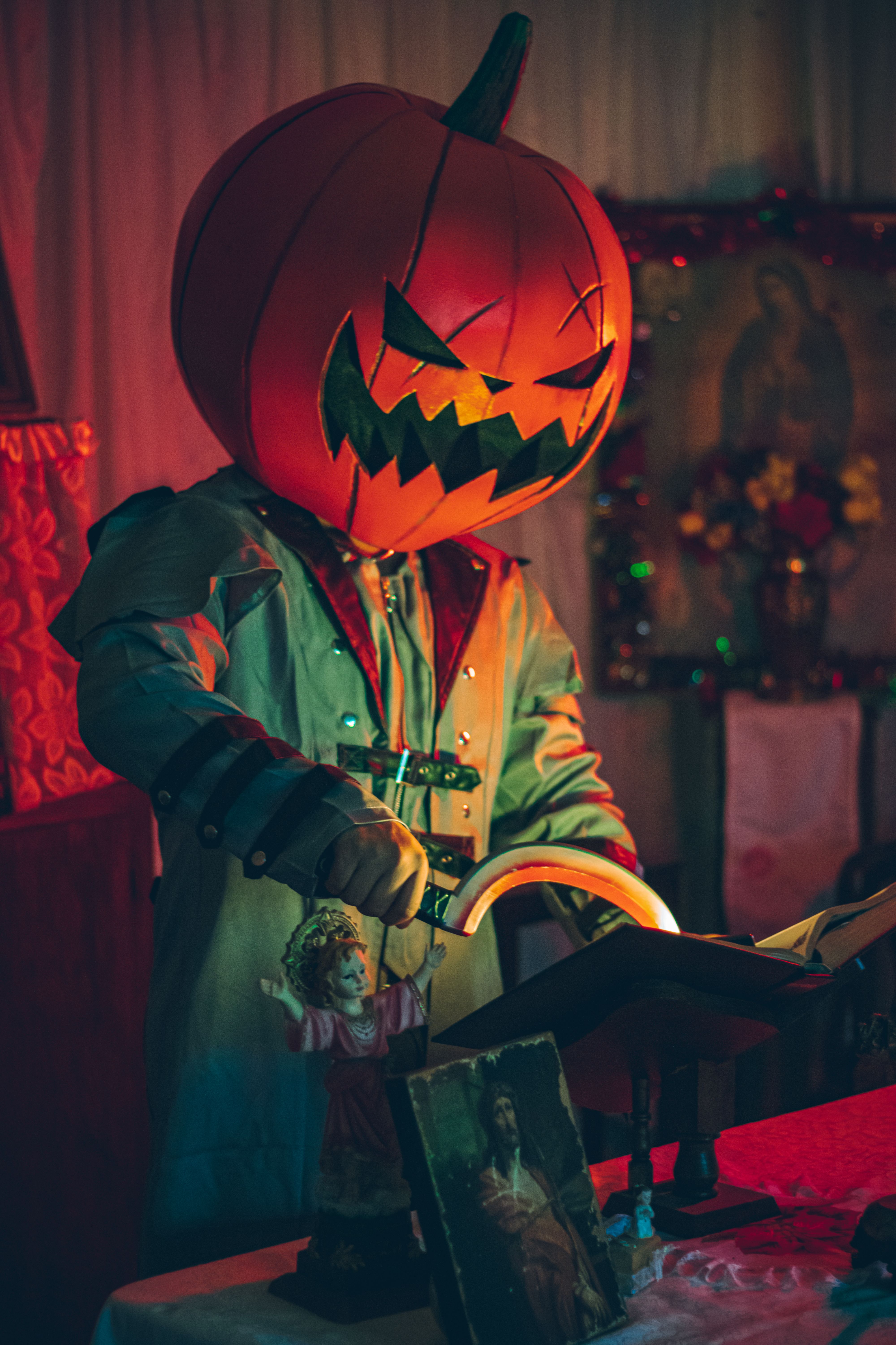 A person in a pumpkin head cosplay reading a book in a dimly lit room with Halloween decorations.