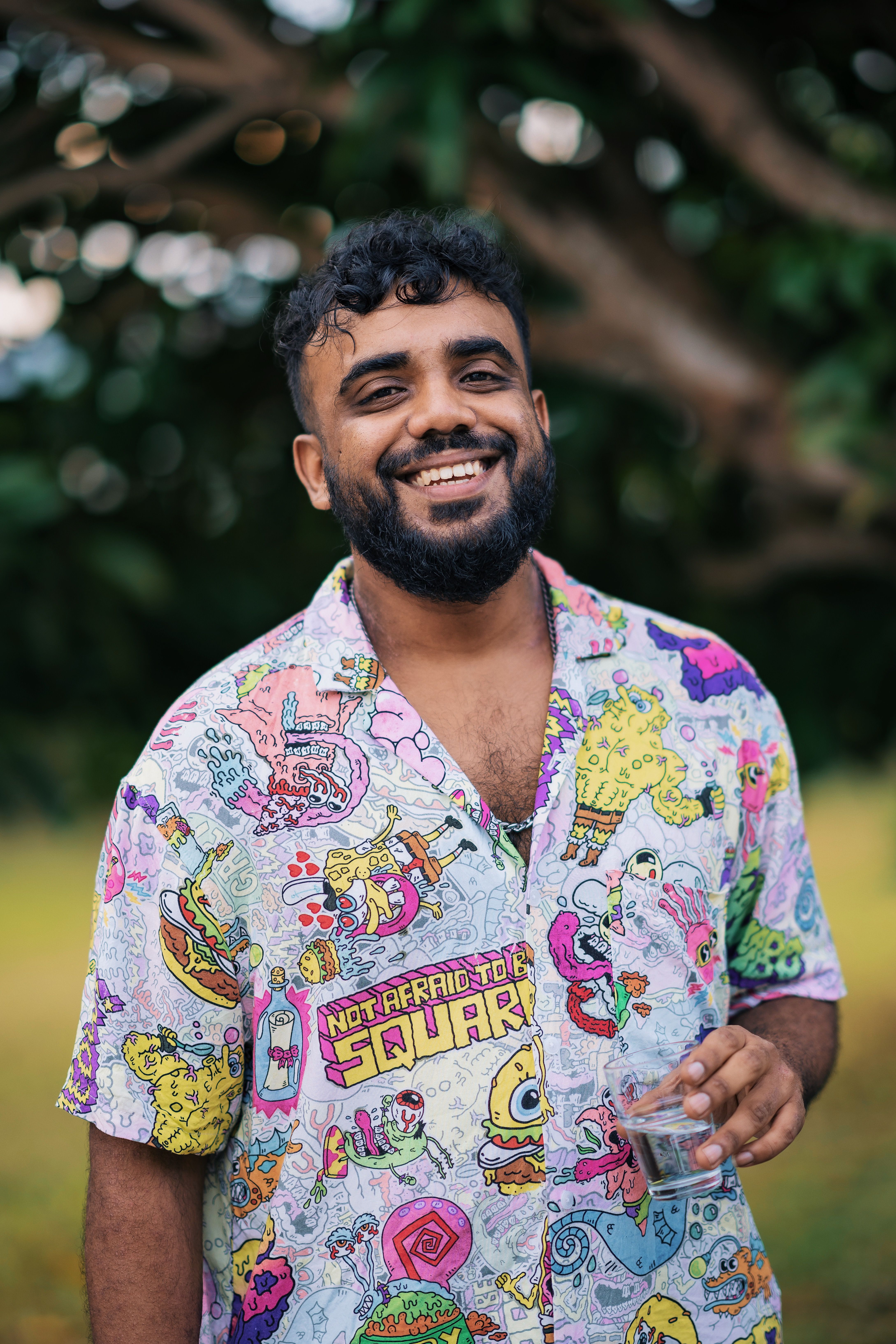 A cheerful man wearing a colorful cartoon print shirt, enjoying an outdoor setting.
