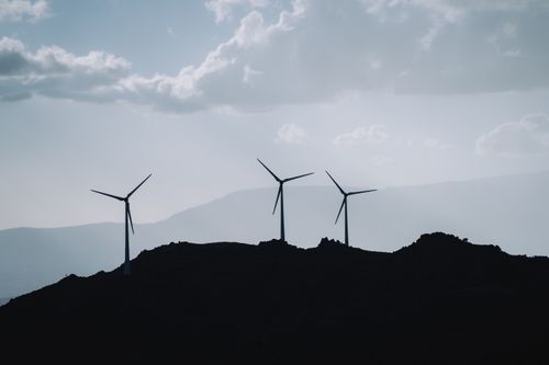 Free Silhouette of three wind turbines on a mountain ridge under a cloudy sky, promoting renewable energy. Stock Photo