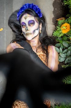 A woman in traditional calavera catrina makeup lies among flowers, celebrating Día de Muertos in Mexico City.