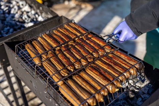 Sausages being grilled outdoors on a barbecue with charcoal.