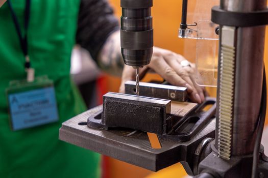 Detailed view of a hand operating a drill press in a workshop setting.