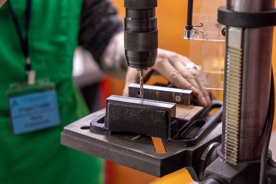 Detailed view of a hand operating a drill press in a workshop setting.