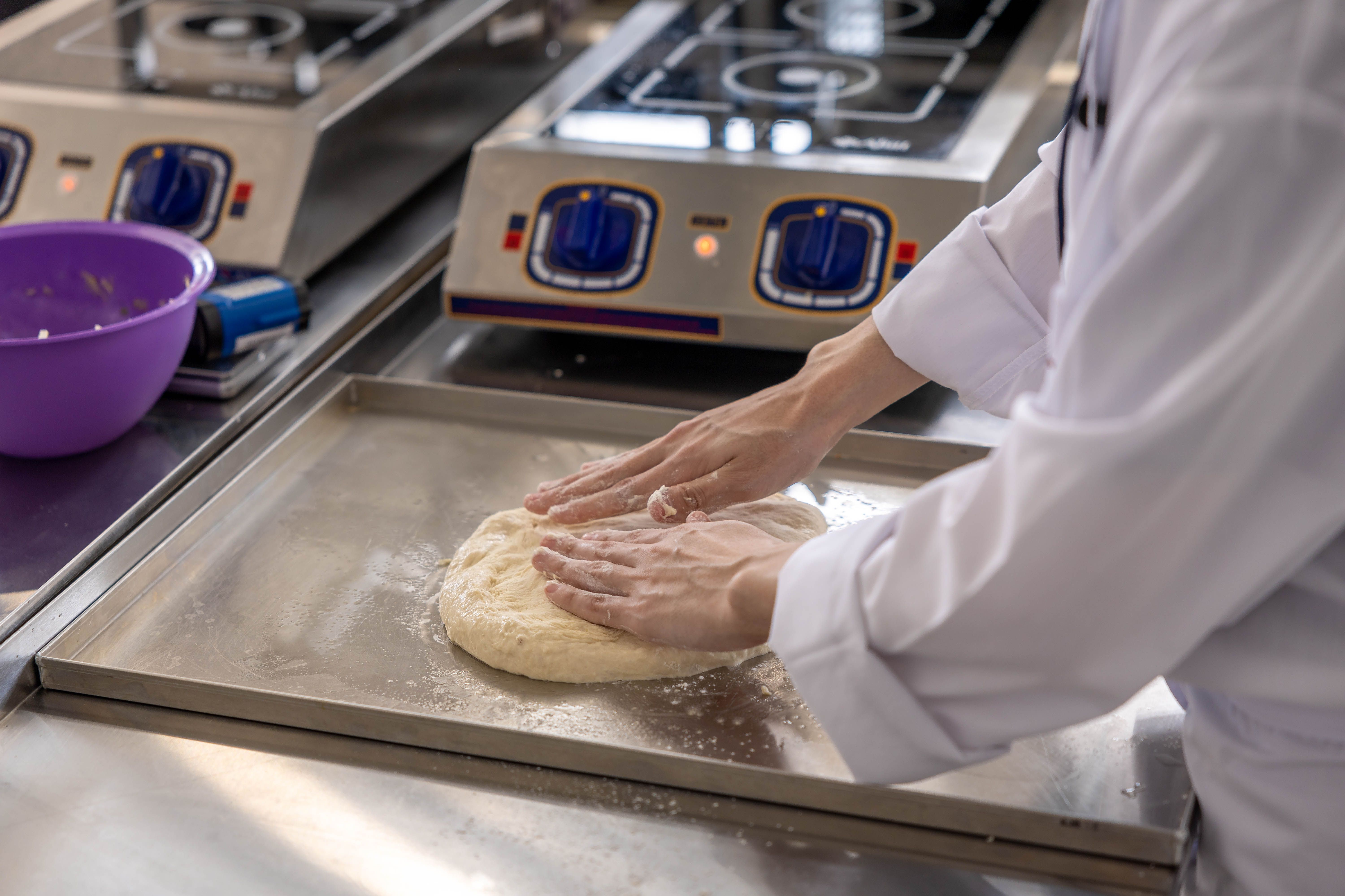 A chef is kneading dough on a stainless steel counter in a commercial kitchen.