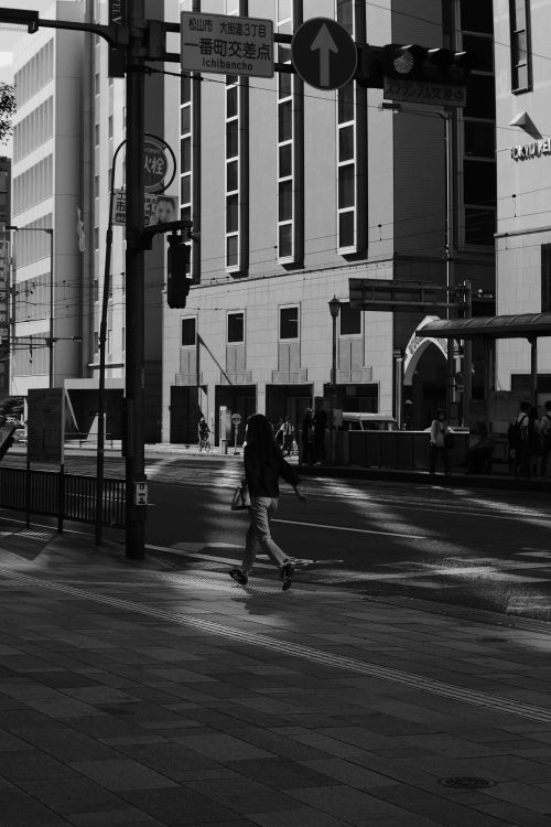 Free Silhouetted person crossing a city street with modern architecture in black and white. Stock Photo