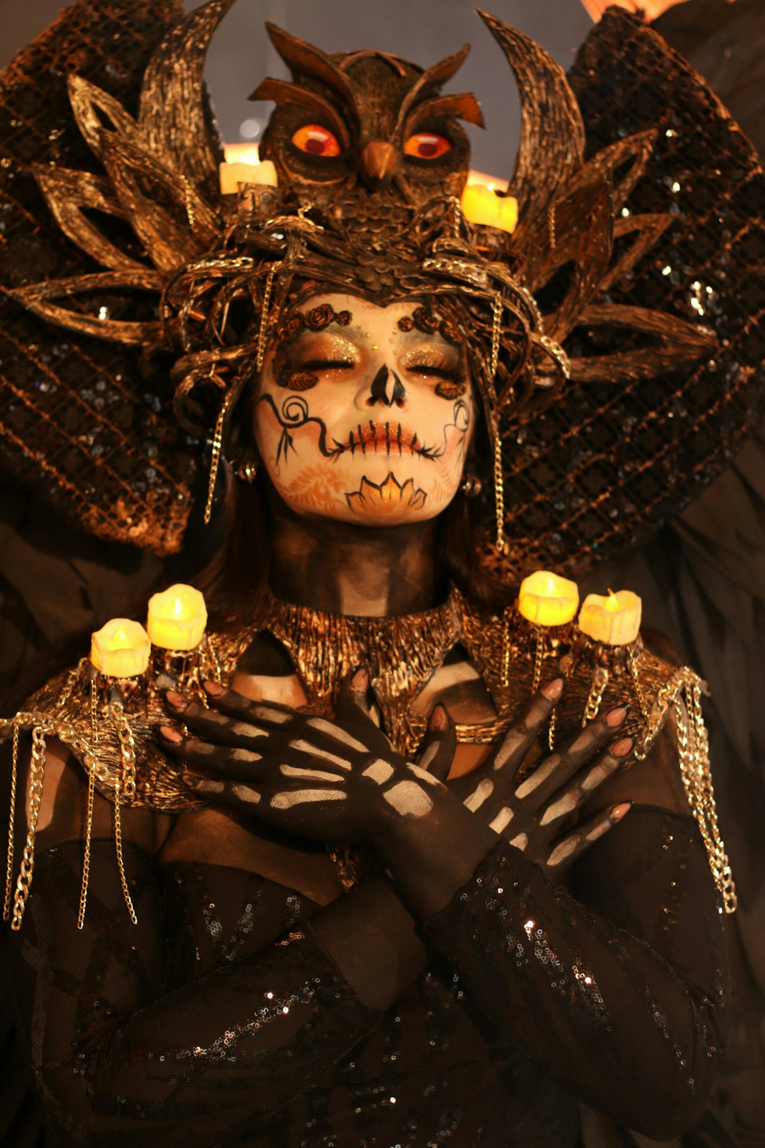 무료 두개골 얼굴 페인트와 정교한 머리 장식이 달린 어둡고 복잡한 의상을 입은 사람. 그 주위는 촛불로 둘러싸여 있습니다. 스톡 사진